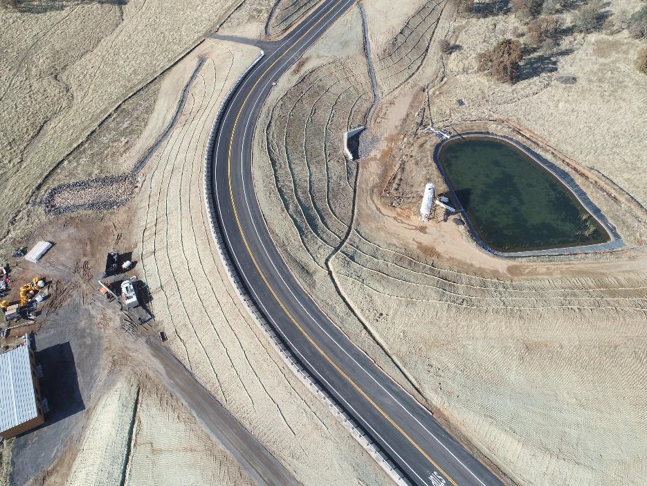 A newly paved road curves past a small pond and construction equipment in a grassy, partially developed landscape.